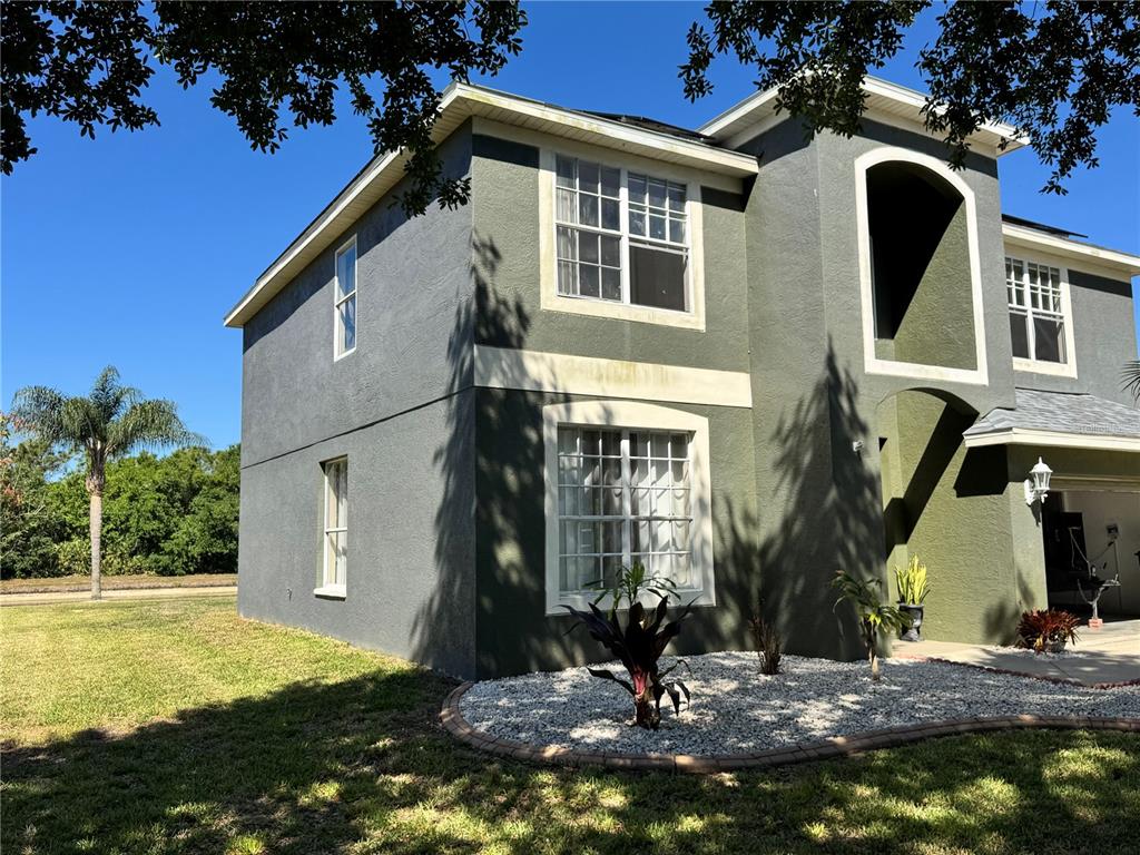 A two-story house with dark green stucco siding, white trim, and a gravel garden bed — 9023 PINEBREEZE DRIVE, RIVERVIEW, FL