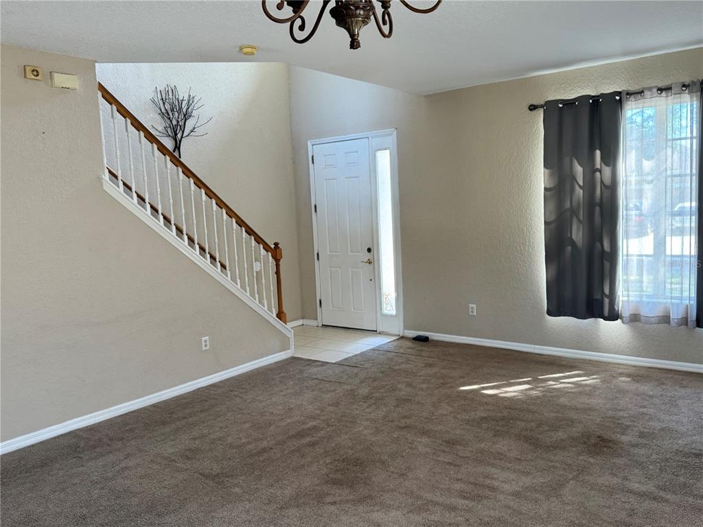 A living room with beige walls, brown carpeting, a staircase, and a front entry door — 9023 PINEBREEZE DRIVE, RIVERVIEW, FL