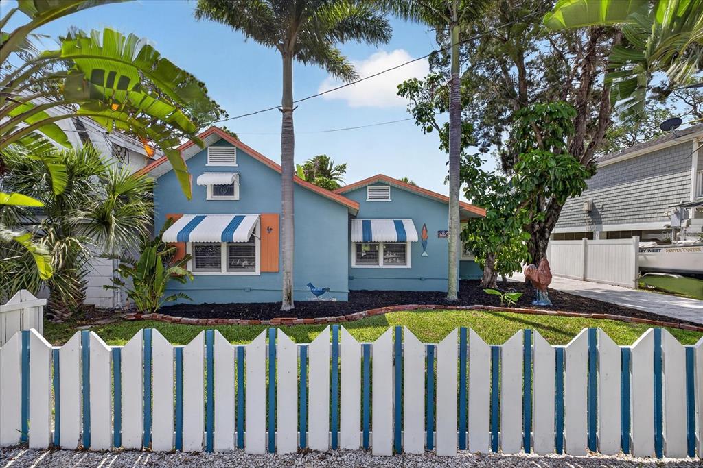 A blue cottage with striped awnings sits behind a white and blue picket fence — 6202 RIVER ROAD, NEW PORT RICHEY, FL
