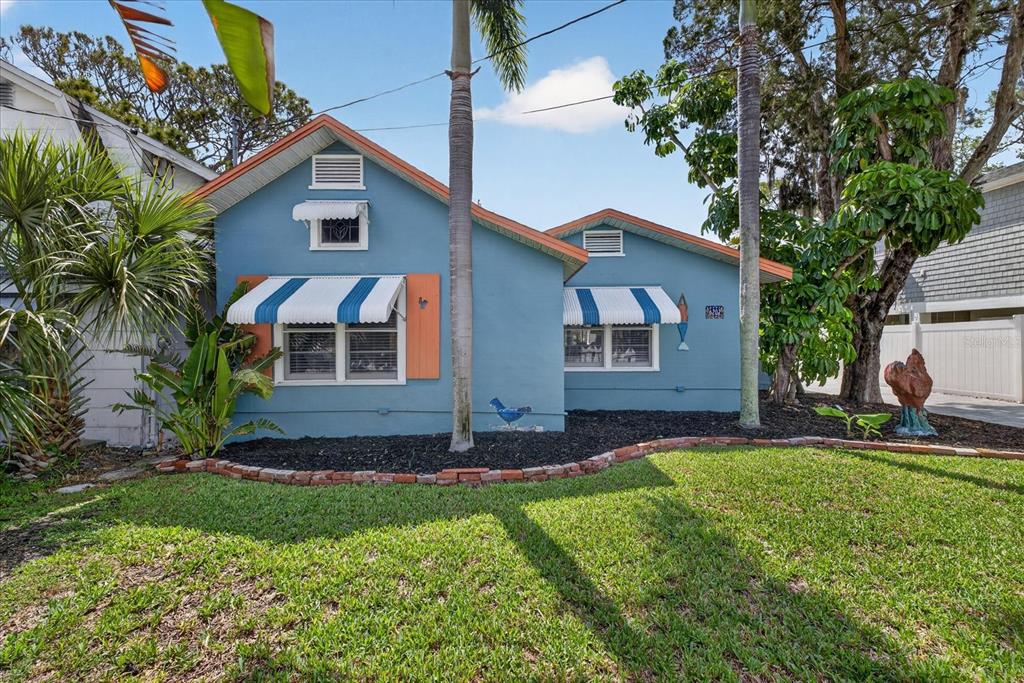 A blue single-story house features white-and-blue striped window awnings and a brick-bordered garden bed — 6202 RIVER ROAD, NEW PORT RICHEY, FL