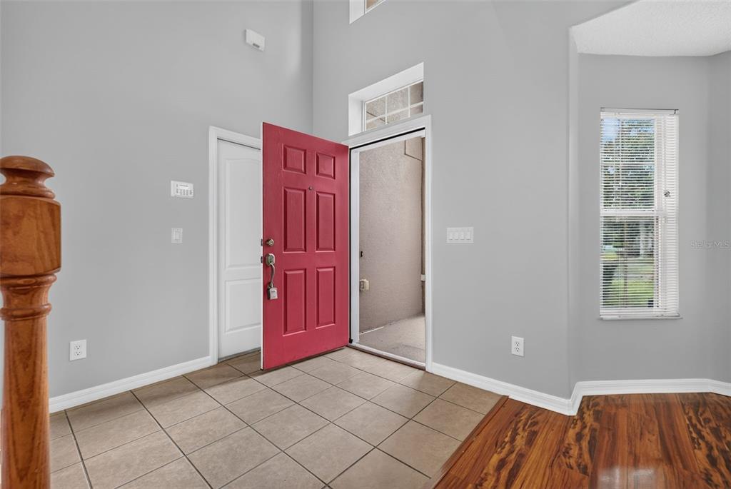 An entryway features a red front door, tiled flooring, and a view of an outdoor porch — 9931 HERON POINTE DRIVE, ORLANDO, FL