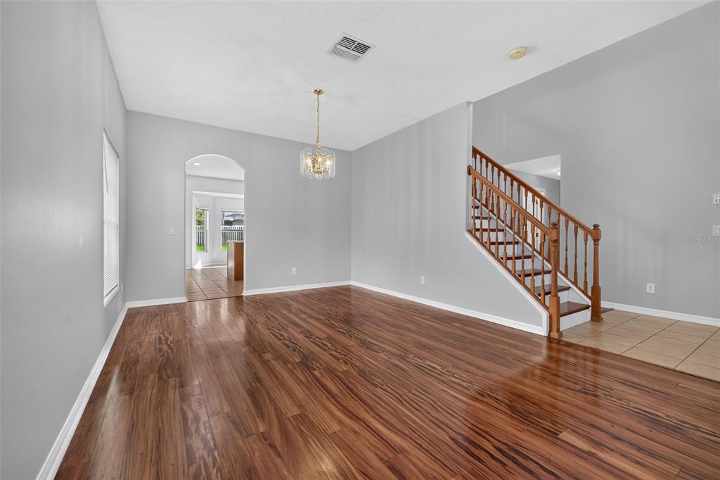 An empty room with wood-look flooring, gray walls, a chandelier, and a wooden staircase — 9931 HERON POINTE DRIVE, ORLANDO, FL