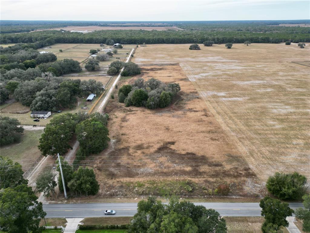 An aerial view shows a large, dry grassy field bordered by trees and a paved road — TBD SW 140TH AVENUE, DUNNELLON, FL