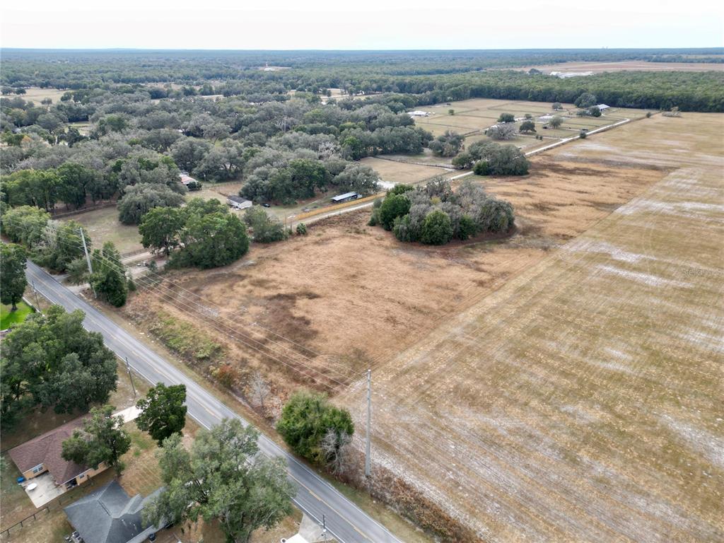 An aerial view shows a large, dry, grassy lot bordering a paved road and trees — TBD SW 140TH AVENUE, DUNNELLON, FL