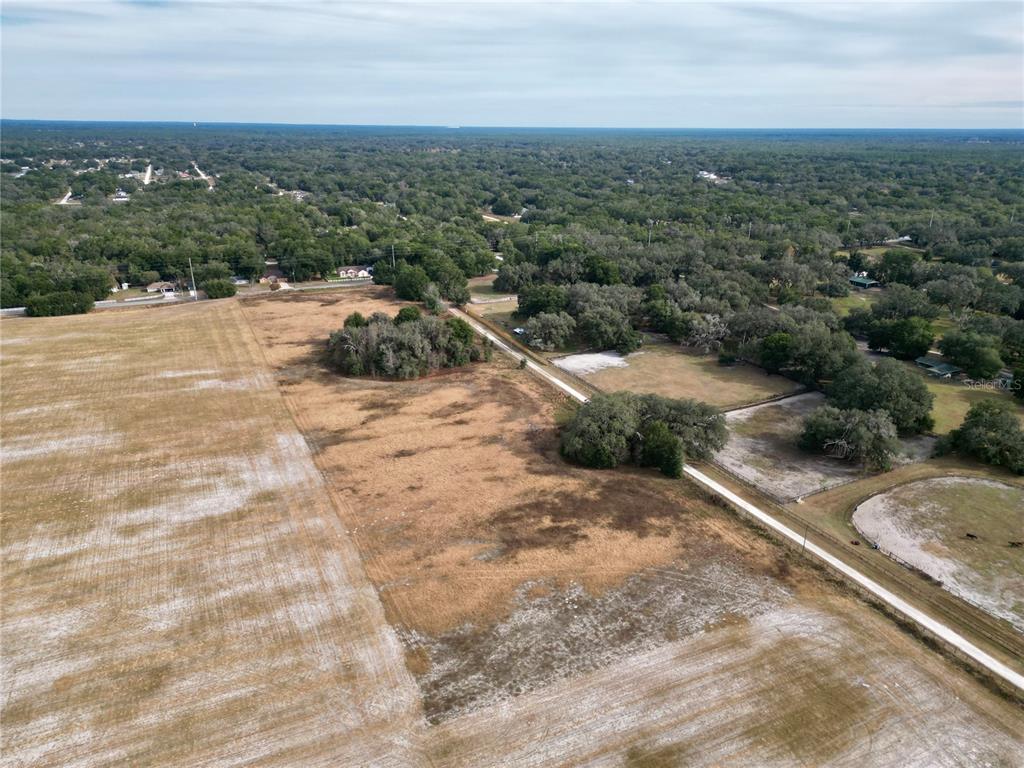An aerial view shows a large, dry grassy field bordered by trees and a dirt road — TBD SW 140TH AVENUE, DUNNELLON, FL