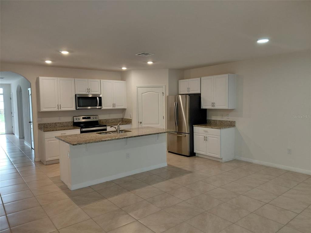 A kitchen features white cabinets, granite countertops, stainless steel appliances, and tile flooring — 1842 EGRET MEADOWS AVENUE, KISSIMMEE, FL