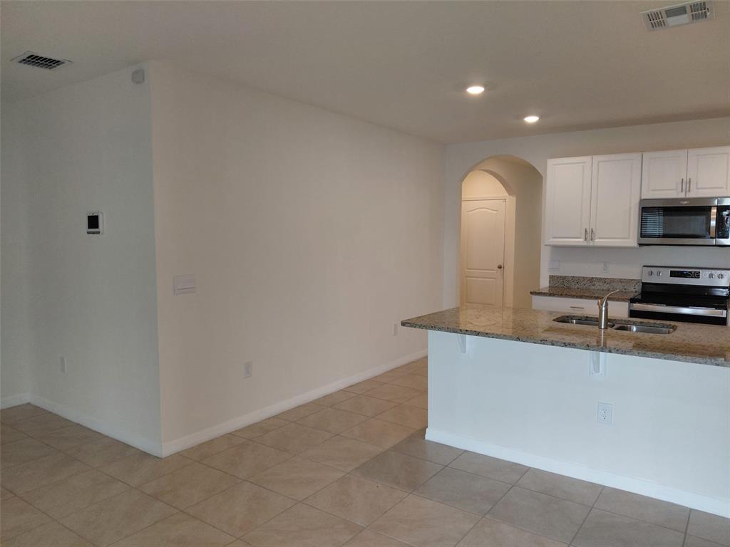 A kitchen with white cabinets, granite countertops, and tile flooring opens to an adjacent room — 1842 EGRET MEADOWS AVENUE, KISSIMMEE, FL