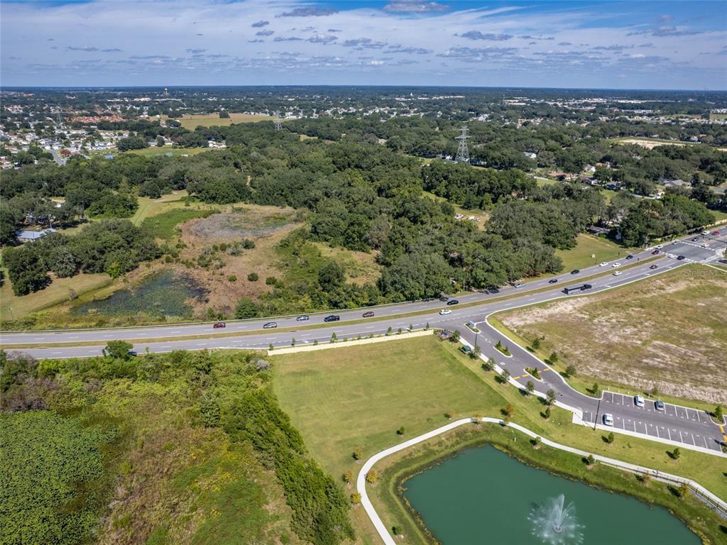 An aerial view shows a pond with a fountain, a grassy lot, and a nearby highway — 8924 E C-466, THE VILLAGES, FL
