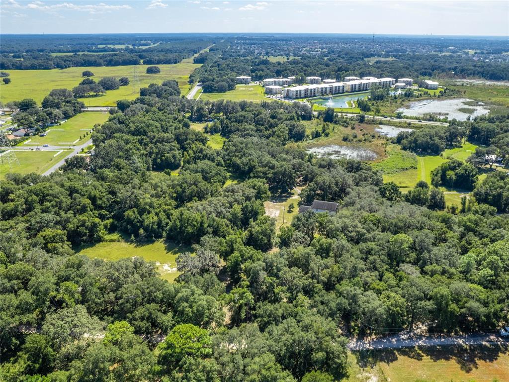 An aerial view shows a house surrounded by dense trees, fields, and a nearby apartment complex — 8924 E C-466, THE VILLAGES, FL