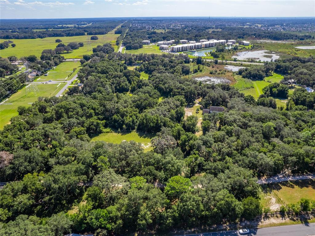 An aerial view shows a large, wooded lot with a house surrounded by dense trees — 8924 E C-466, THE VILLAGES, FL