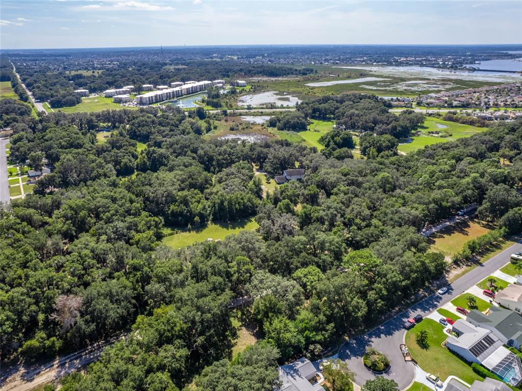 An aerial view shows a wooded lot with a house surrounded by trees and nearby neighborhoods — 8924 E C-466, THE VILLAGES, FL