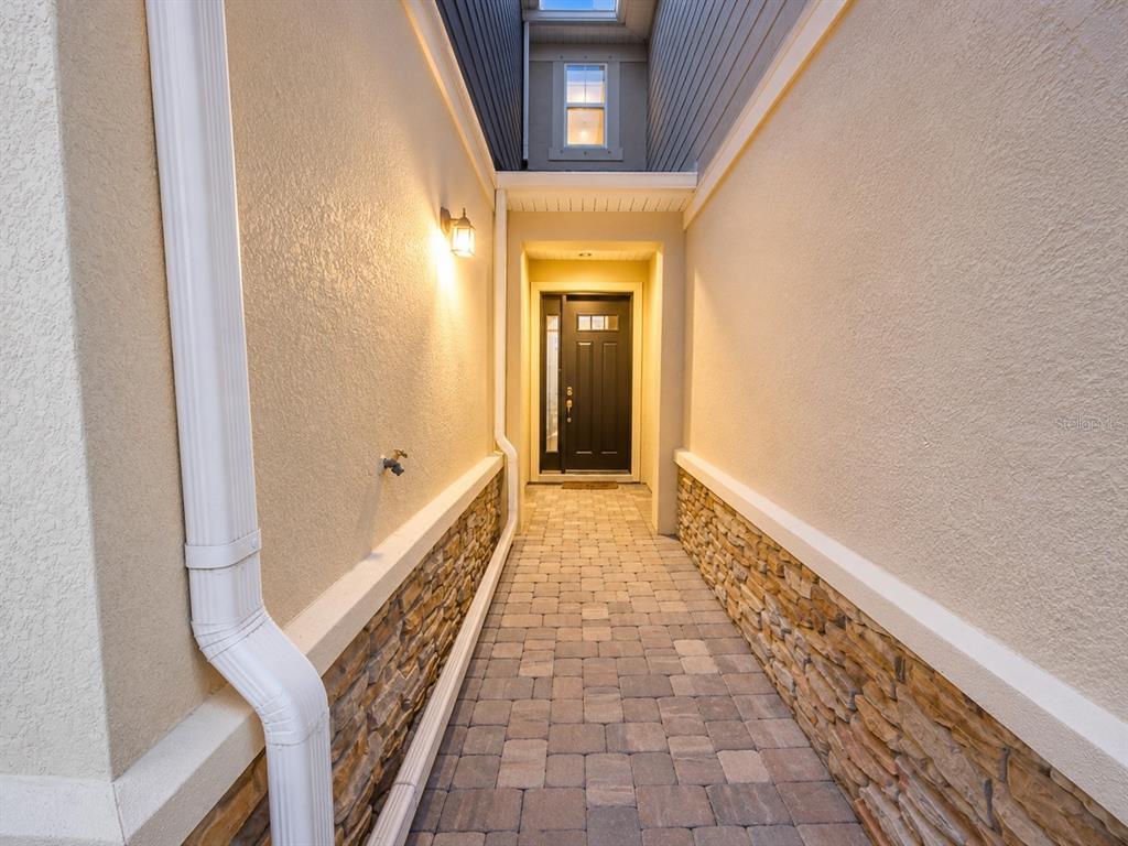 A paved walkway leads to a dark front door between two stucco walls with stone accents — 12365 TRAILHEAD DRIVE, LAKEWOOD RANCH, FL