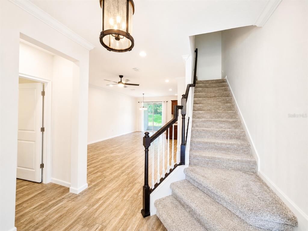 A foyer features wood-look flooring, a staircase with carpeted steps, and a view into a living area — 12365 TRAILHEAD DRIVE, LAKEWOOD RANCH, FL