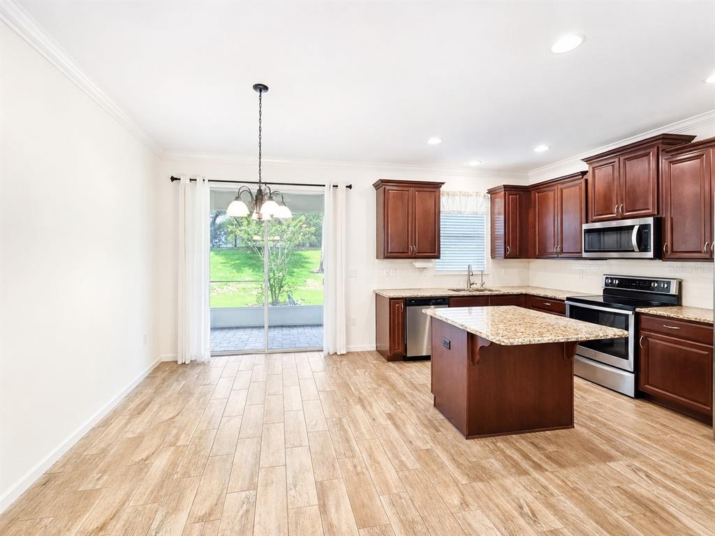 A kitchen and dining area with wood-look tile floors, dark cabinets, and a granite island — 12365 TRAILHEAD DRIVE, LAKEWOOD RANCH, FL