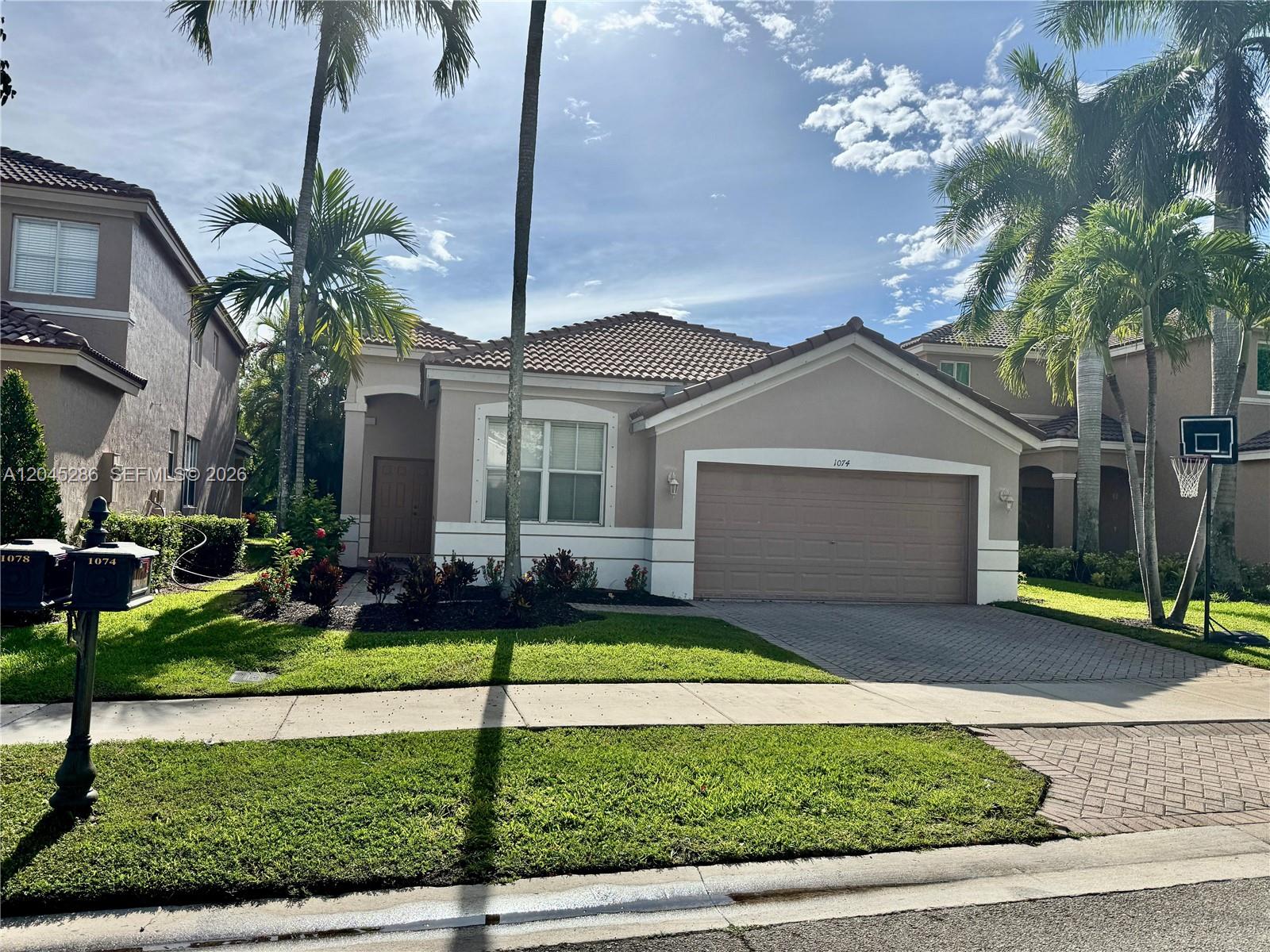 A single-story house with a beige stucco exterior, a tile roof, and a two-car garage — 1074 Bluewood Ter # 0, Weston FL 33327, WESTON, FL