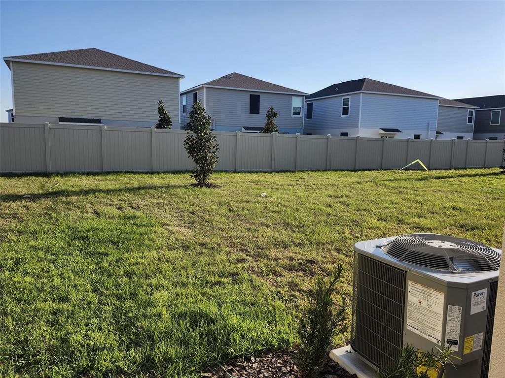 A grassy backyard features a tan vinyl fence and an air conditioning unit — 3898 AMERS LOOP, HAINES CITY, FL