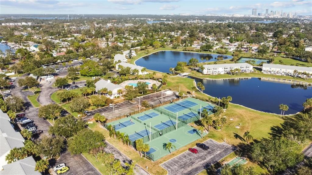An aerial view shows tennis courts, a swimming pool, and lakes within a residential community — 5004 STARFISH DRIVE SE UNIT F, ST PETERSBURG, FL