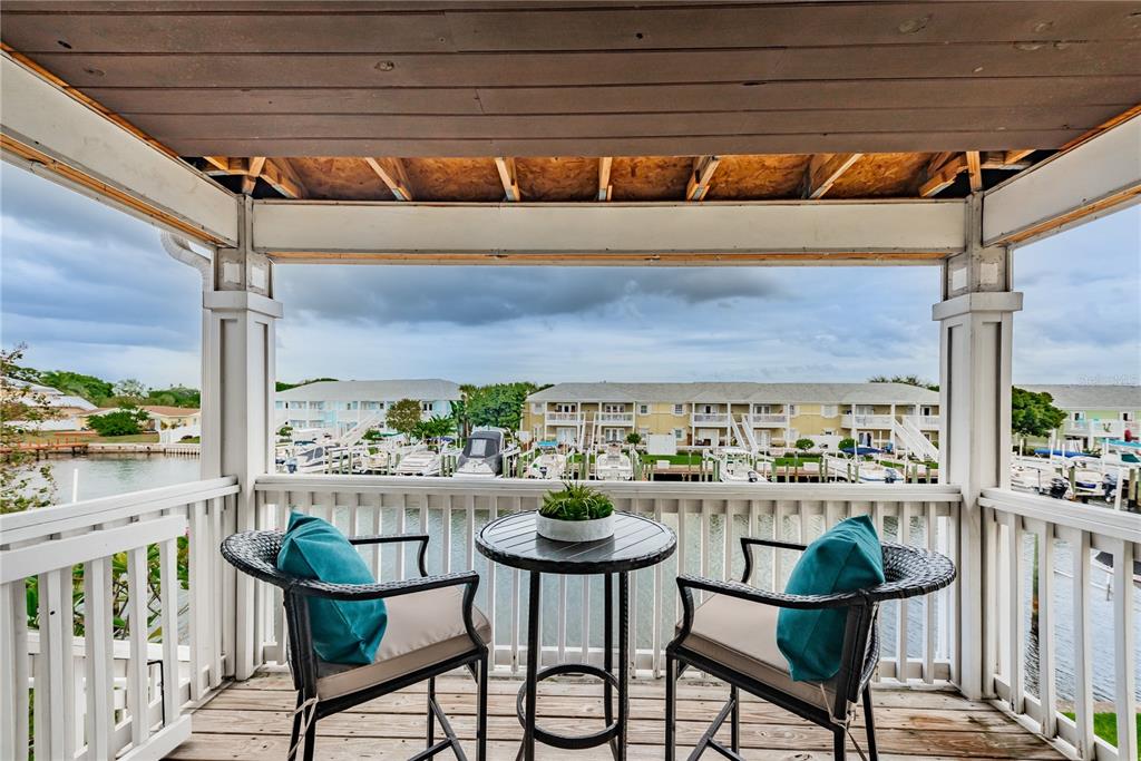 A covered balcony features two chairs, a small table, and a view of a marina — 5004 STARFISH DRIVE SE UNIT F, ST PETERSBURG, FL