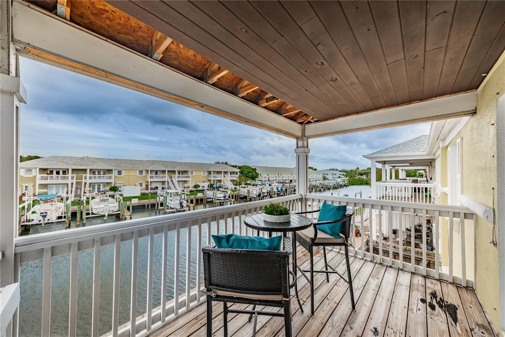 A balcony with a small table and two chairs overlooks a canal with docked boats — 5004 STARFISH DRIVE SE UNIT F, ST PETERSBURG, FL