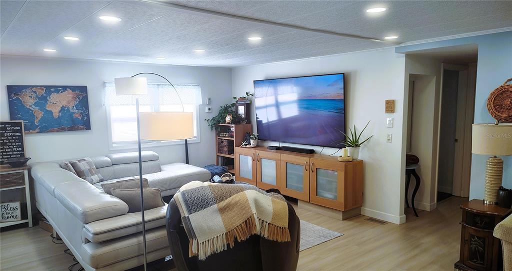 A living room features a large television on a wooden console, sectional sofa, and lighting — 714 48TH B AVENUE E, BRADENTON, FL