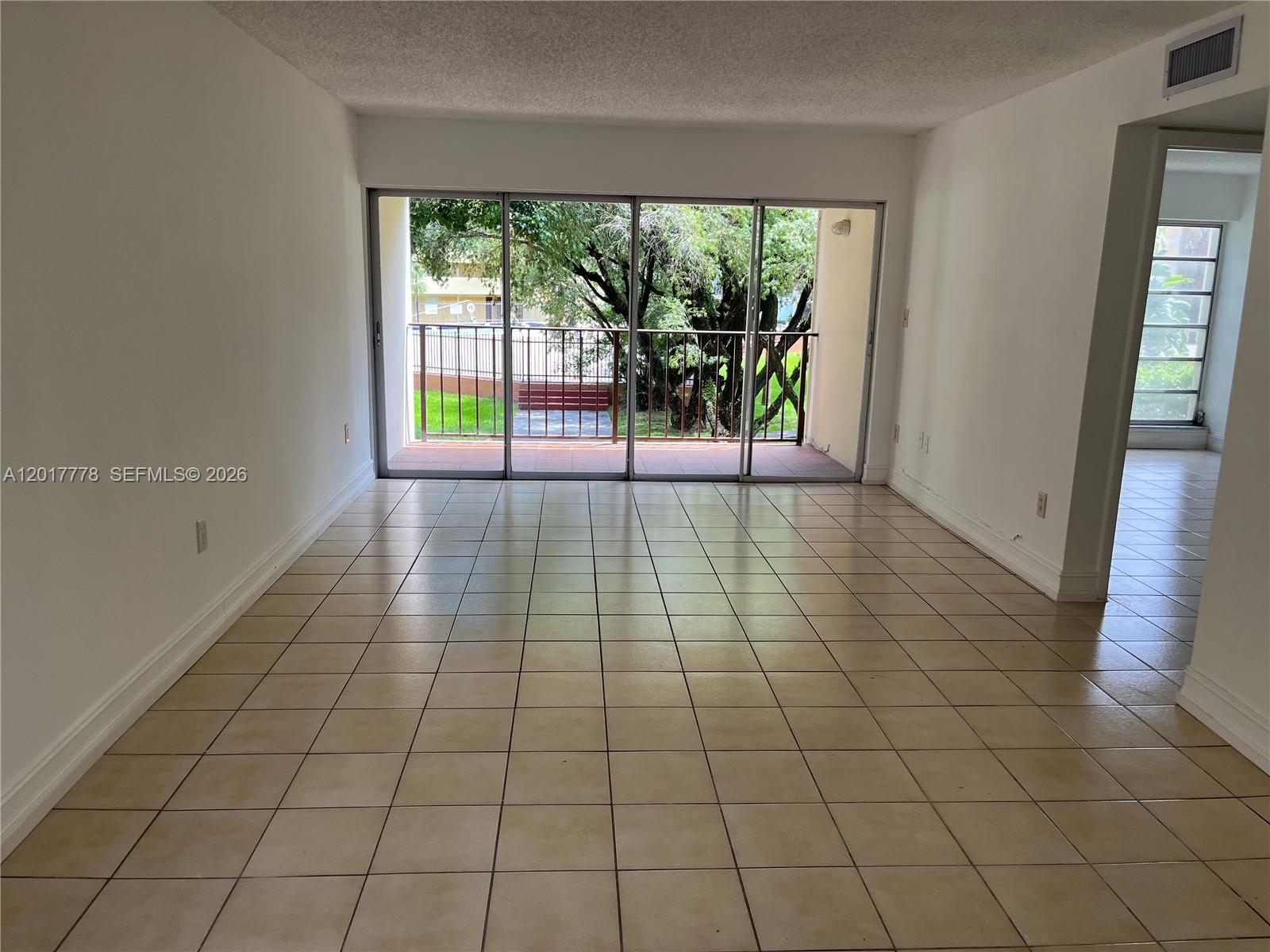 A living area with beige tile flooring features a large sliding glass door to a balcony — 9190 Fontainebleau Blvd # 202, Miami FL 33172, MIAMI, FL
