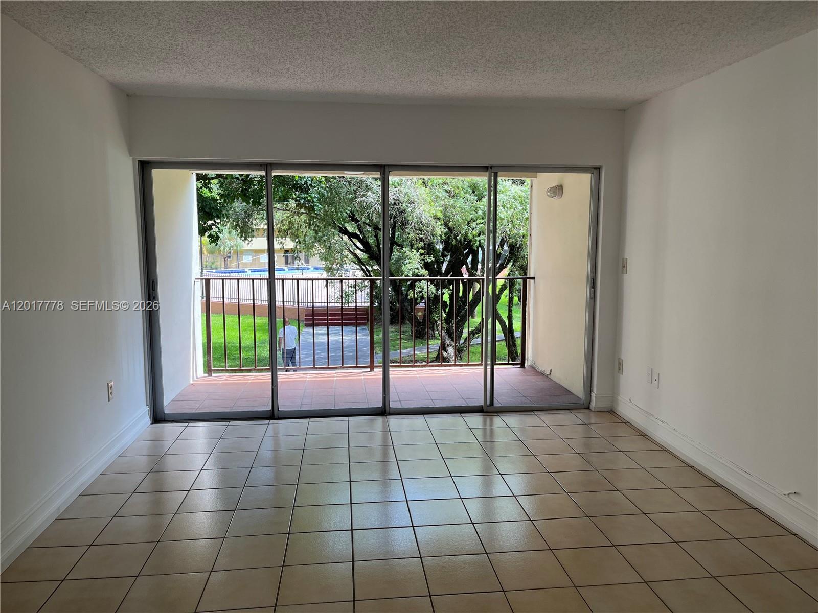 An empty room with beige tile flooring features a large sliding glass door to a balcony — 9190 Fontainebleau Blvd # 202, Miami FL 33172, MIAMI, FL