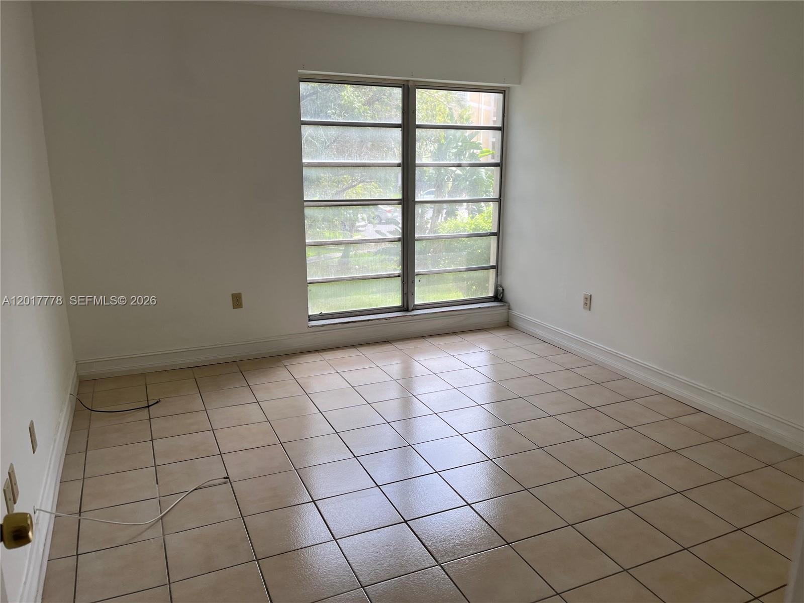 An empty room features white walls, beige tile flooring, and a large multi-pane window — 9190 Fontainebleau Blvd # 202, Miami FL 33172, MIAMI, FL