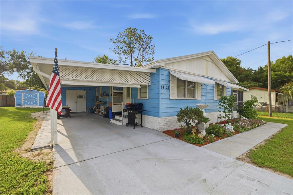 A blue single-story house features a carport, a front garden, and an American flag — 14121 SE 91ST COURT, SUMMERFIELD, FL