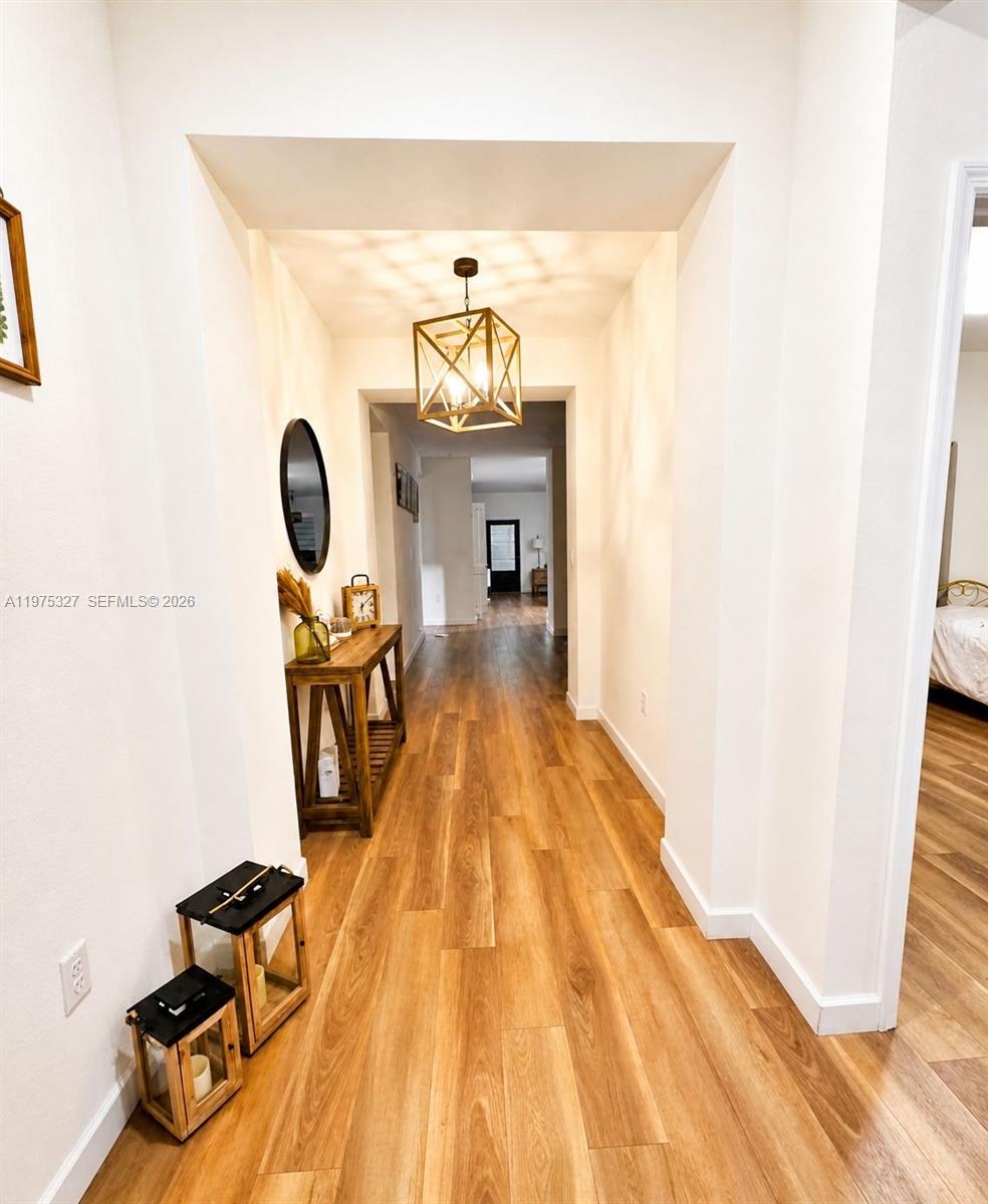 A hallway with wood-look flooring leads to a doorway featuring a geometric pendant light — 24341 SW 118th Path, Homestead FL 33032, HOMESTEAD, FL
