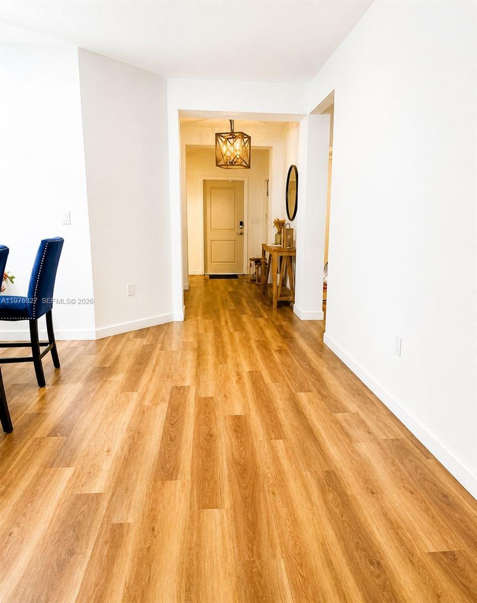 A hallway with wood-look flooring leads to an entryway door under a geometric pendant light — 24341 SW 118th Path, Homestead FL 33032, HOMESTEAD, FL