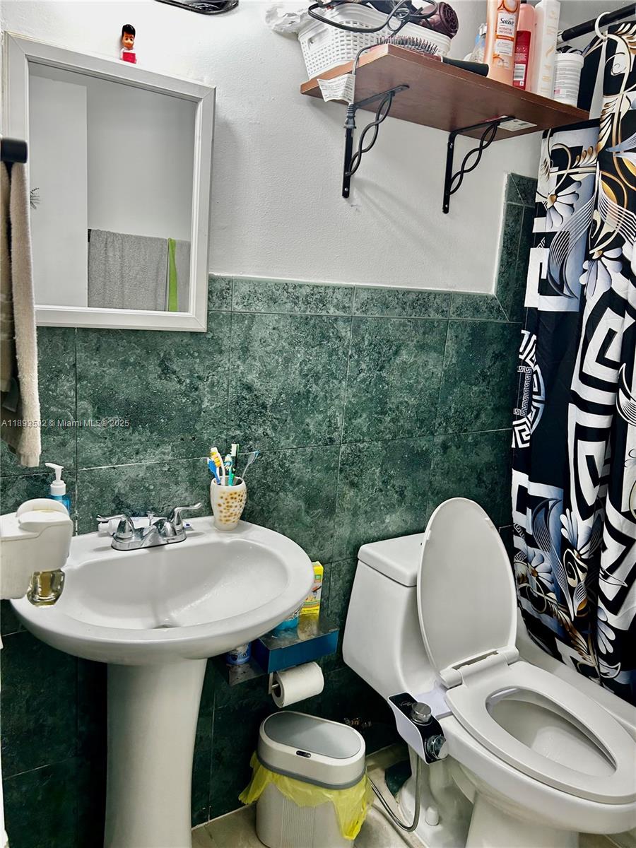 A bathroom features a pedestal sink, a toilet with a bidet, and green tiled walls — 2918 Funston St # 29B, Hollywood FL 33020, HOLLYWOOD, FL