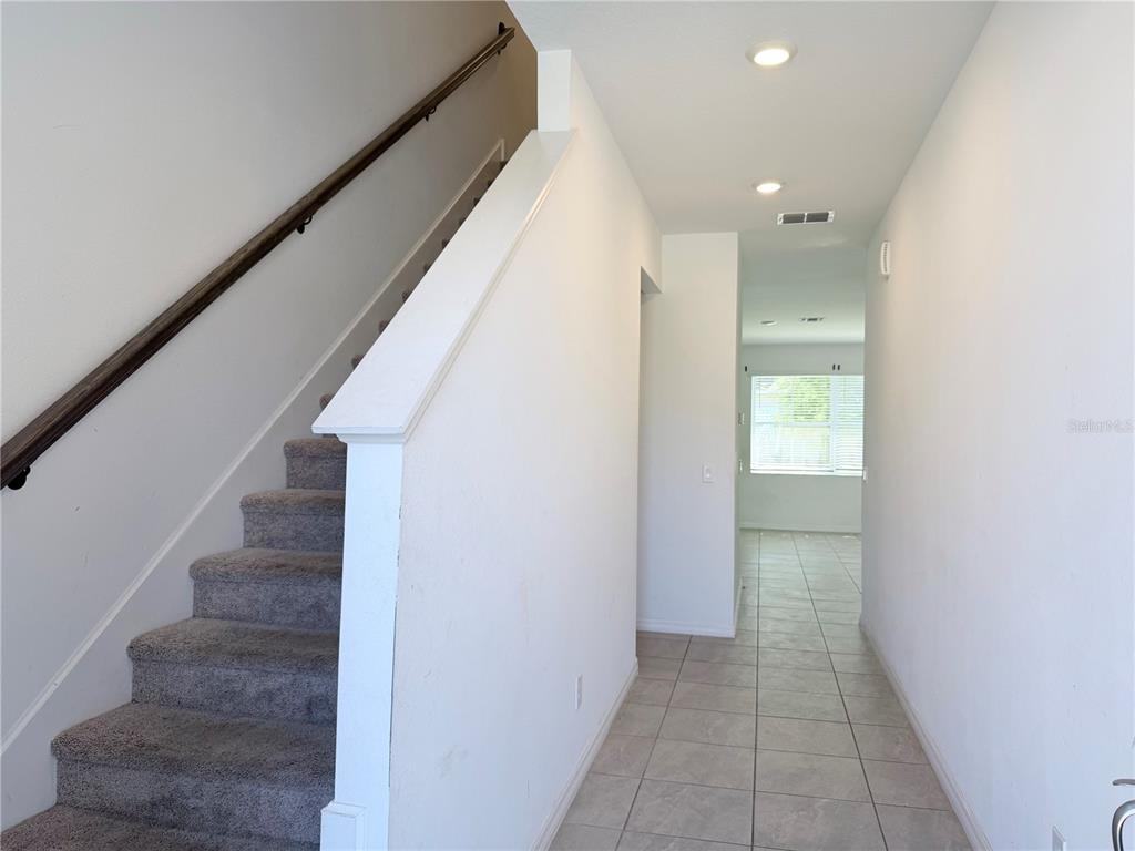 A carpeted staircase with a wooden handrail sits beside a tiled hallway leading to a window — 1542 DISCOVERY STREET, DAVENPORT, FL