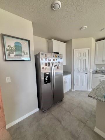 A kitchen features a stainless steel refrigerator, white cabinets, and light-colored tile flooring — 384 GUADLUPE STREET, HAINES CITY, FL