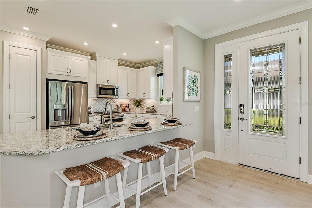 A kitchen with granite countertops, white cabinets, and three bar stools near an entryway door — 14541 DERNA TERRACE, BRADENTON, FL