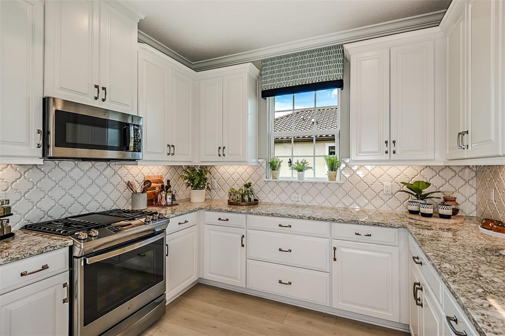 A kitchen features white cabinets, granite countertops, a stainless steel stove, and a patterned backsplash — 14541 DERNA TERRACE, BRADENTON, FL