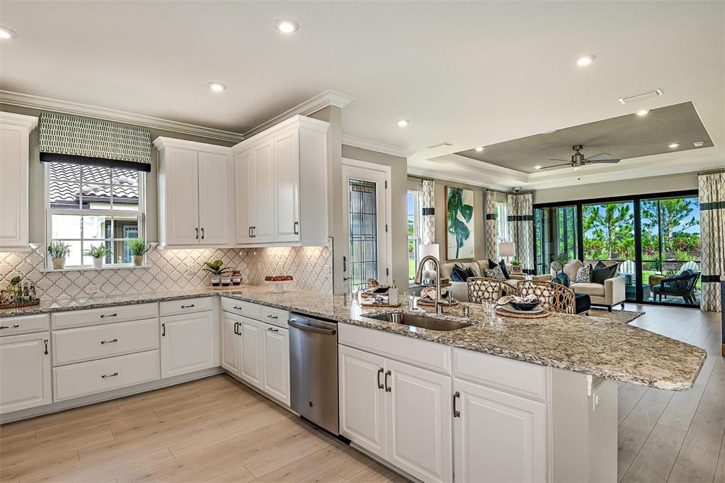 A bright kitchen with white cabinets, granite countertops, and an island overlooks a living area — 14541 DERNA TERRACE, BRADENTON, FL