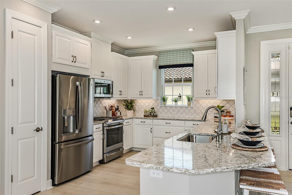 A modern kitchen features white cabinetry, stainless steel appliances, and a granite-topped island — 14541 DERNA TERRACE, BRADENTON, FL