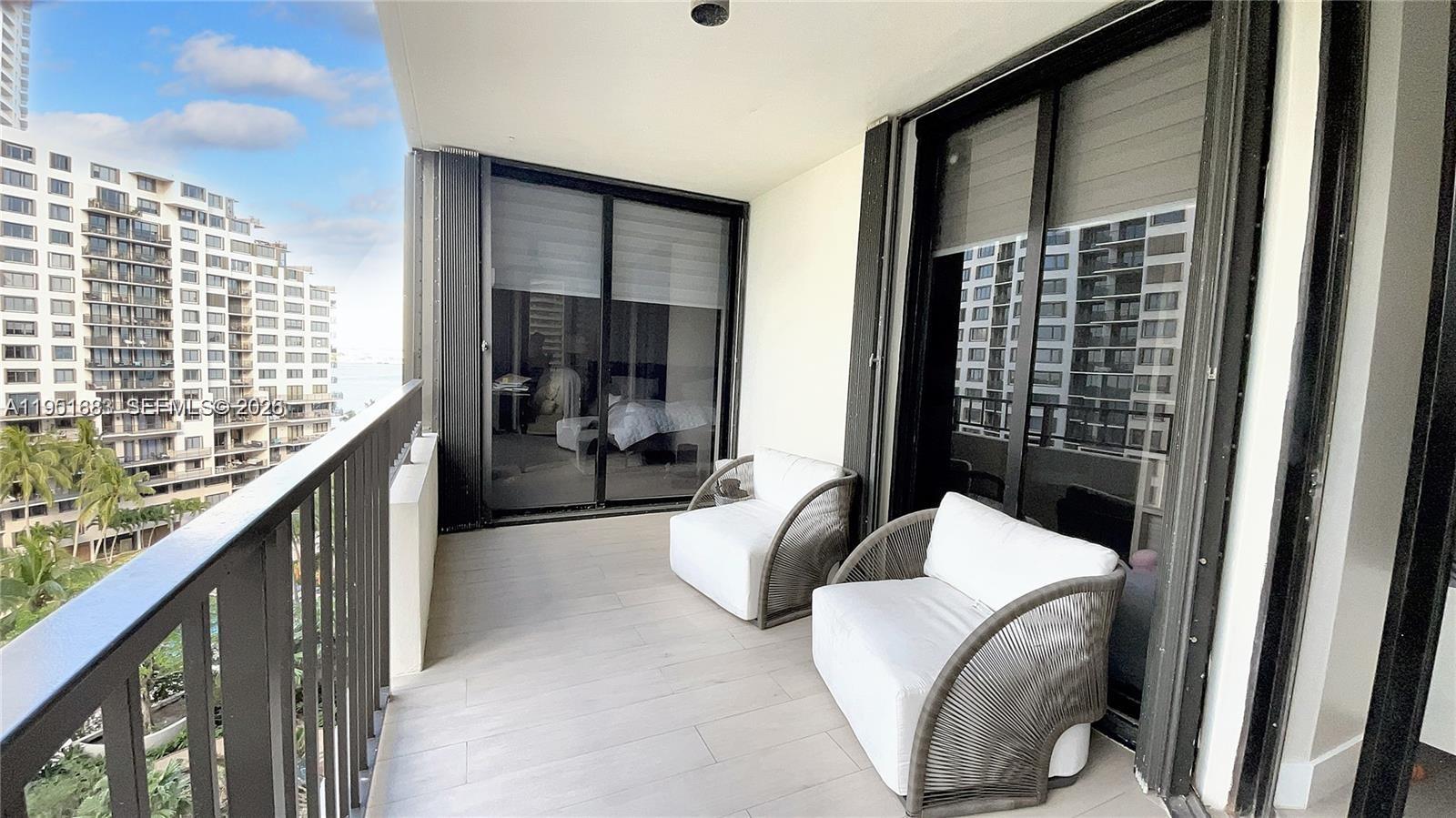 A balcony features two white armchairs, light-colored tile flooring, and a view of nearby buildings — 520 Brickell Key Dr # A1010, Miami FL 33131, MIAMI, FL