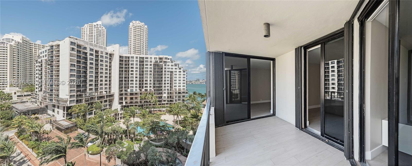 A balcony with light-colored tile flooring overlooks a tropical courtyard and nearby high-rise buildings — 520 Brickell Key Dr # A1010, Miami FL 33131, MIAMI, FL