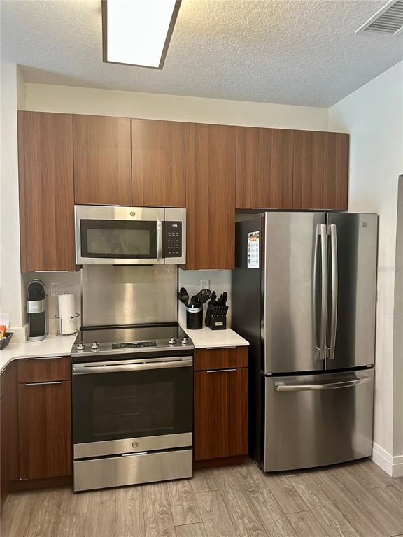 A kitchen features wood-grain cabinets, stainless steel appliances, and light-colored countertops — 14501 GROVE RESORT AVENUE UNIT 2101, WINTER GARDEN, FL