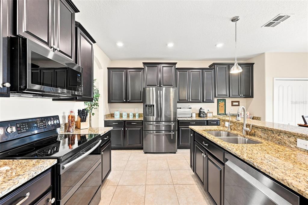 A kitchen features dark wood cabinets, granite countertops, and stainless steel appliances — 12335 BALLENTRAE FOREST DRIVE, RIVERVIEW, FL