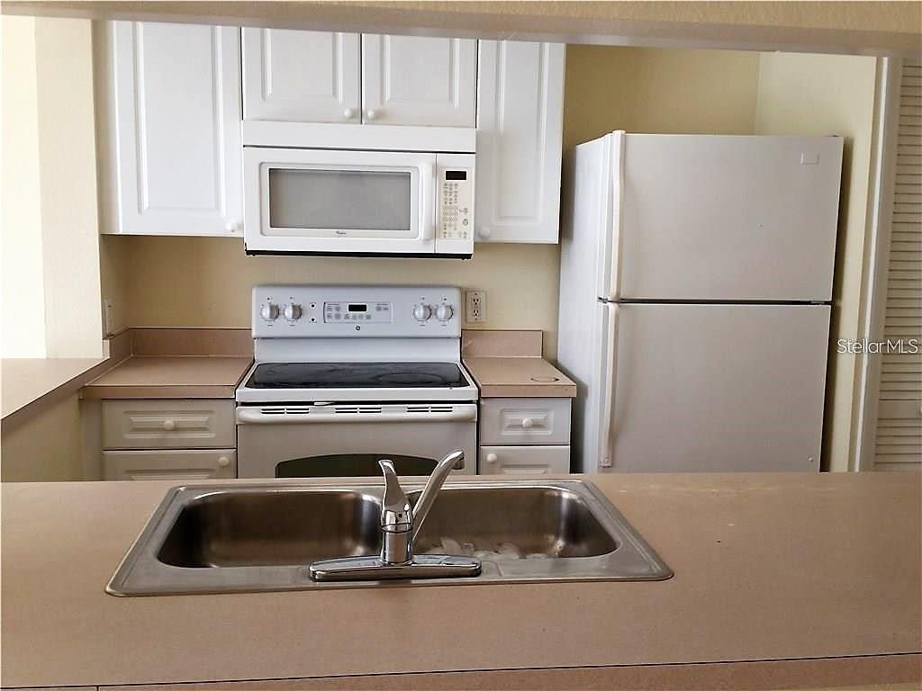 A kitchen features white cabinets, a microwave, a stove, a refrigerator, and a double sink — 251 CARIBBEAN DRIVE, DAVENPORT, FL