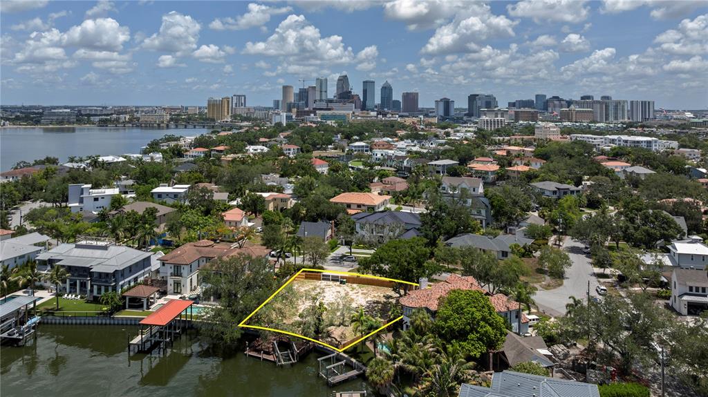 An aerial view shows a vacant waterfront lot outlined in yellow near a city skyline — 86 BAHAMA CIRCLE, TAMPA, FL