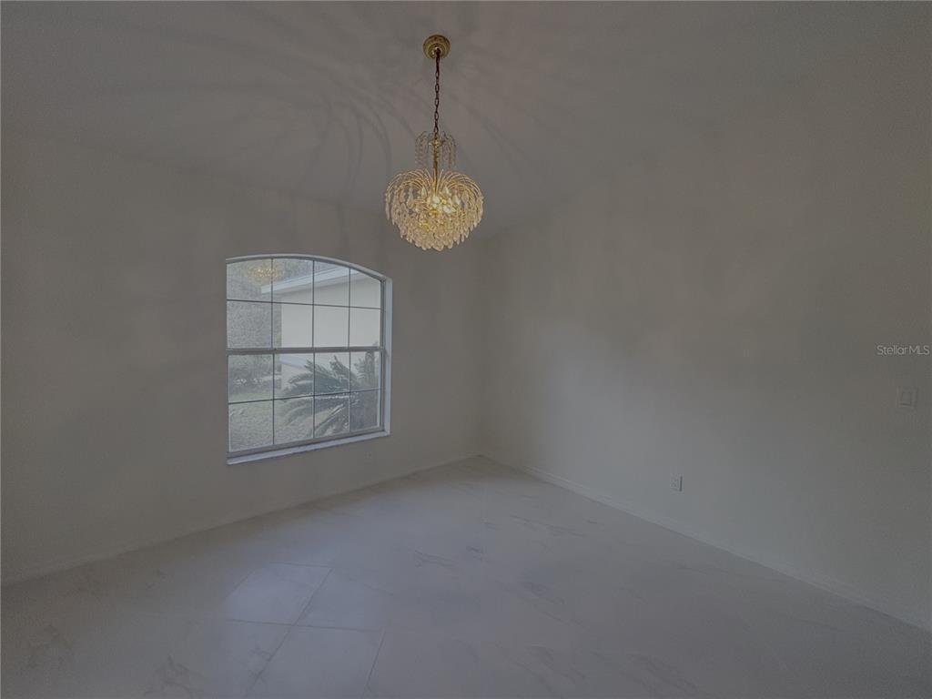 An empty room features white tile flooring, a crystal chandelier, and an arched window — 11435 SW 140TH AVENUE, DUNNELLON, FL
