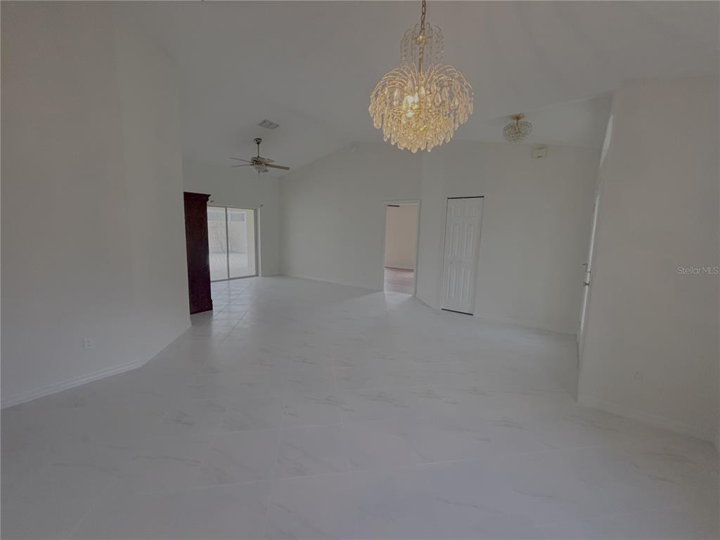A bright, open-concept living area features white tile flooring, a vaulted ceiling, and two chandeliers — 11435 SW 140TH AVENUE, DUNNELLON, FL