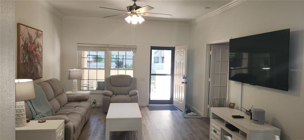 A living room features a grey sofa, armchair, white coffee table, and a wall-mounted television — 304 LOS PRADOS UNIT 304, SAFETY HARBOR, FL