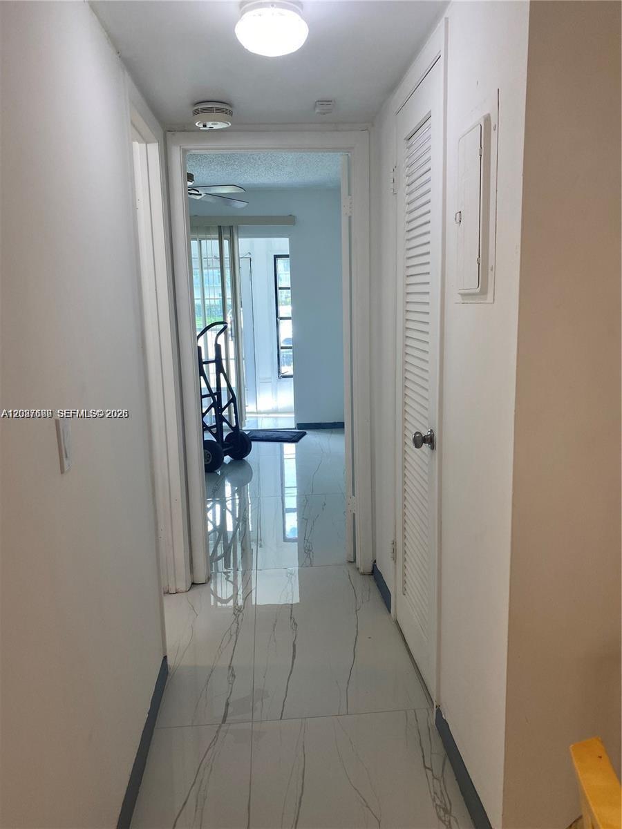 A hallway with white tile flooring leads to a room with a sliding glass door — 111 Tilford F # 111, Deerfield Beach FL 33442, DEERFIELD BEACH, FL