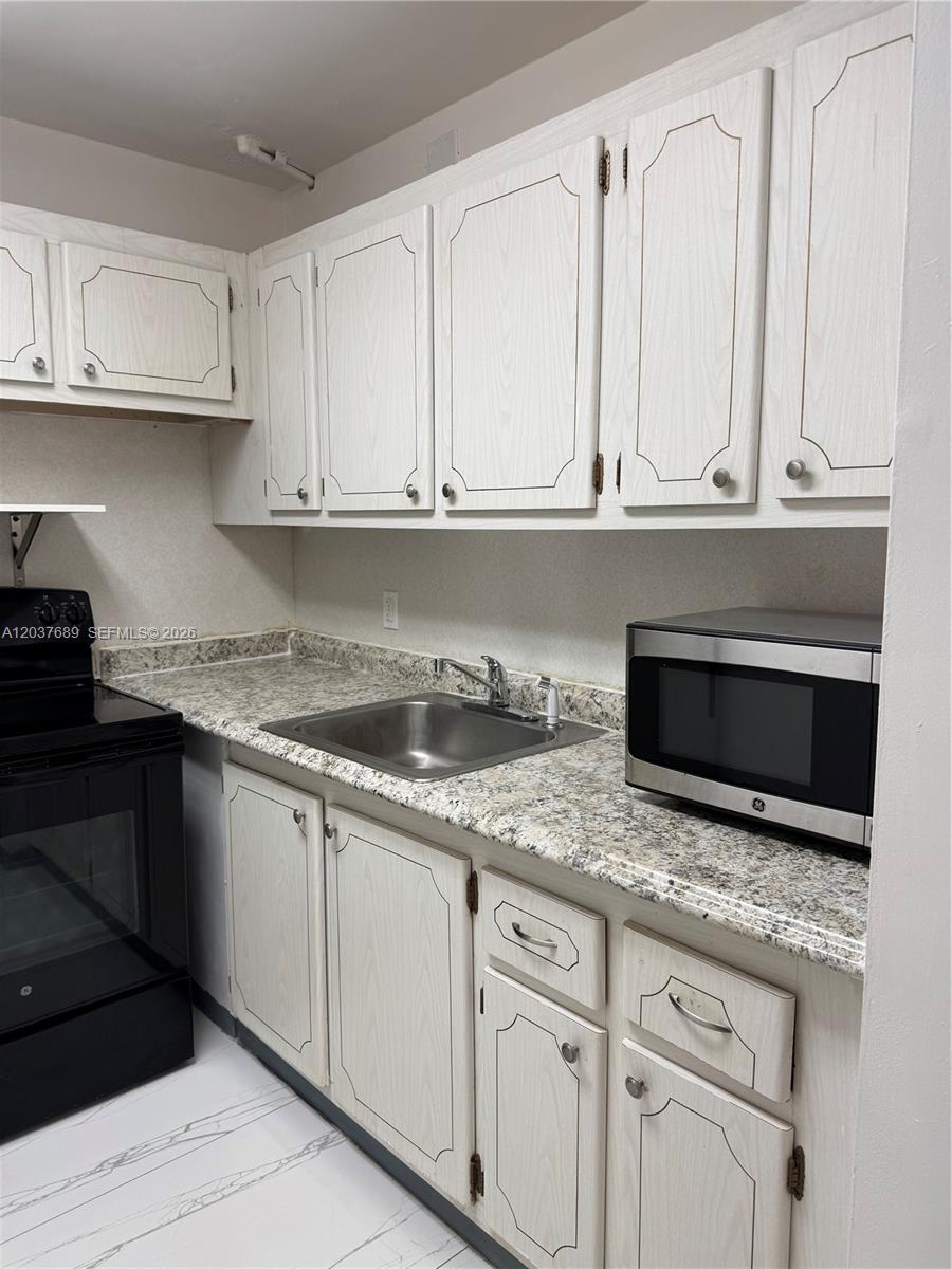 A kitchen features white wood-grain cabinets, a granite-look countertop, and a stainless steel microwave — 111 Tilford F # 111, Deerfield Beach FL 33442, DEERFIELD BEACH, FL