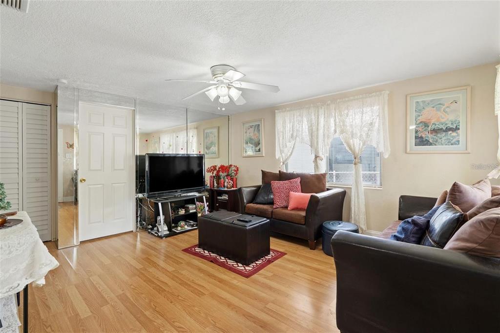 A living room features wood-look flooring, a mirrored wall, a ceiling fan, and brown furniture — 4530 72ND AVENUE N, PINELLAS PARK, FL