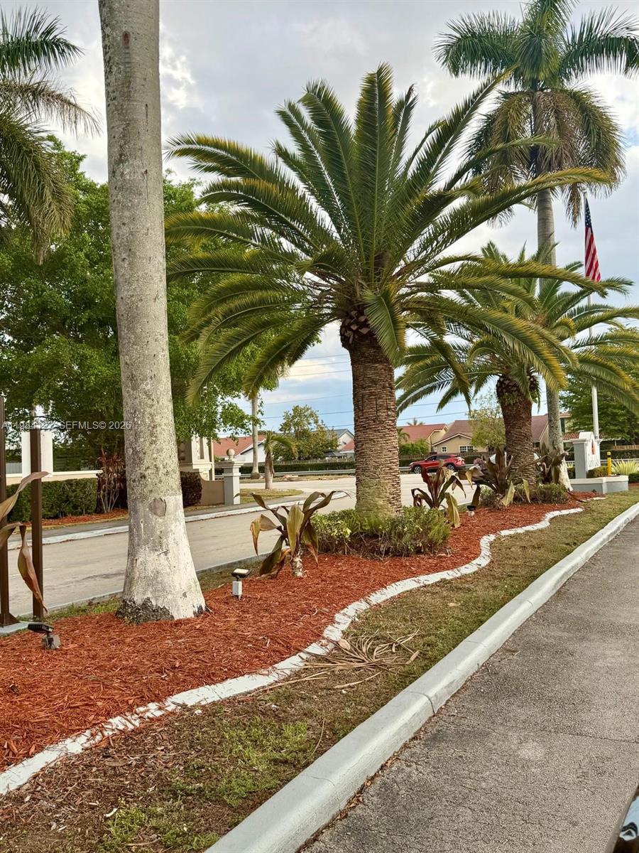 A landscaped entrance features palm trees, red mulch, and a paved road under a cloudy sky — 3858 SW 153rd Pl, Miami FL 33185, MIAMI, FL